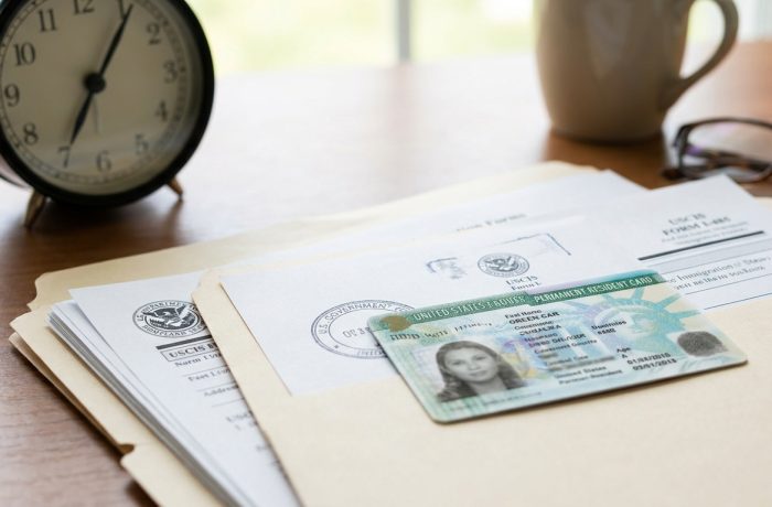 Documentos de inmigracion apilados con Green Card en la parte superior, simbolizando cuanto tarda en llegar la green card y la espera.