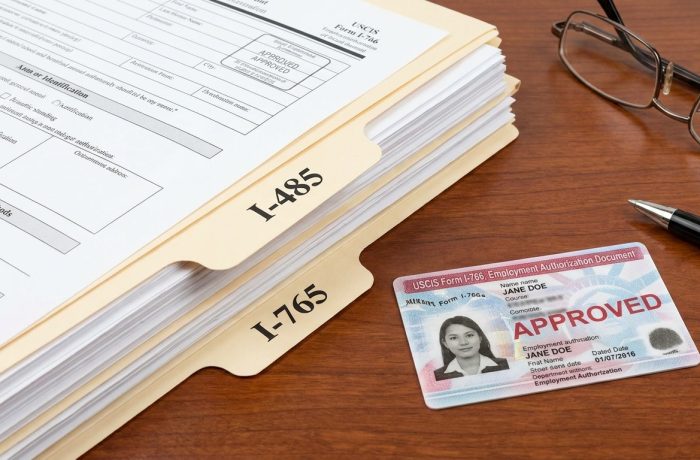 Documentos de inmigracion, incluyendo el formulario I-485 y la tarjeta de permiso de trabajo categoria c09, sobre un escritorio.
