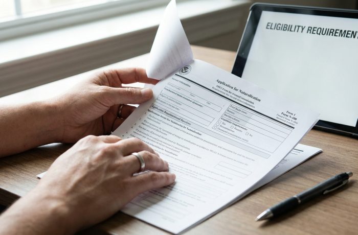 examen ciudadania ingles: Manos revisando un formulario N-400 junto a una tableta y un boligrafo, preparandose para el examen.