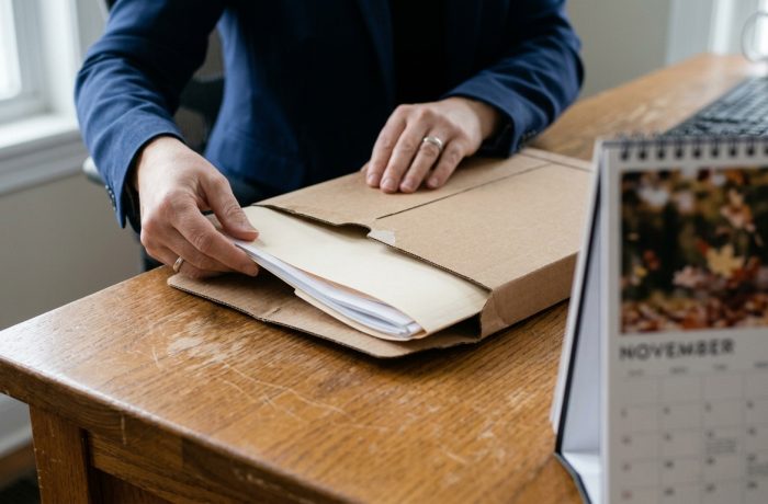 Manos rotulando un paquete postal con la direccion de envio Formulario I-129 sobre un escritorio.